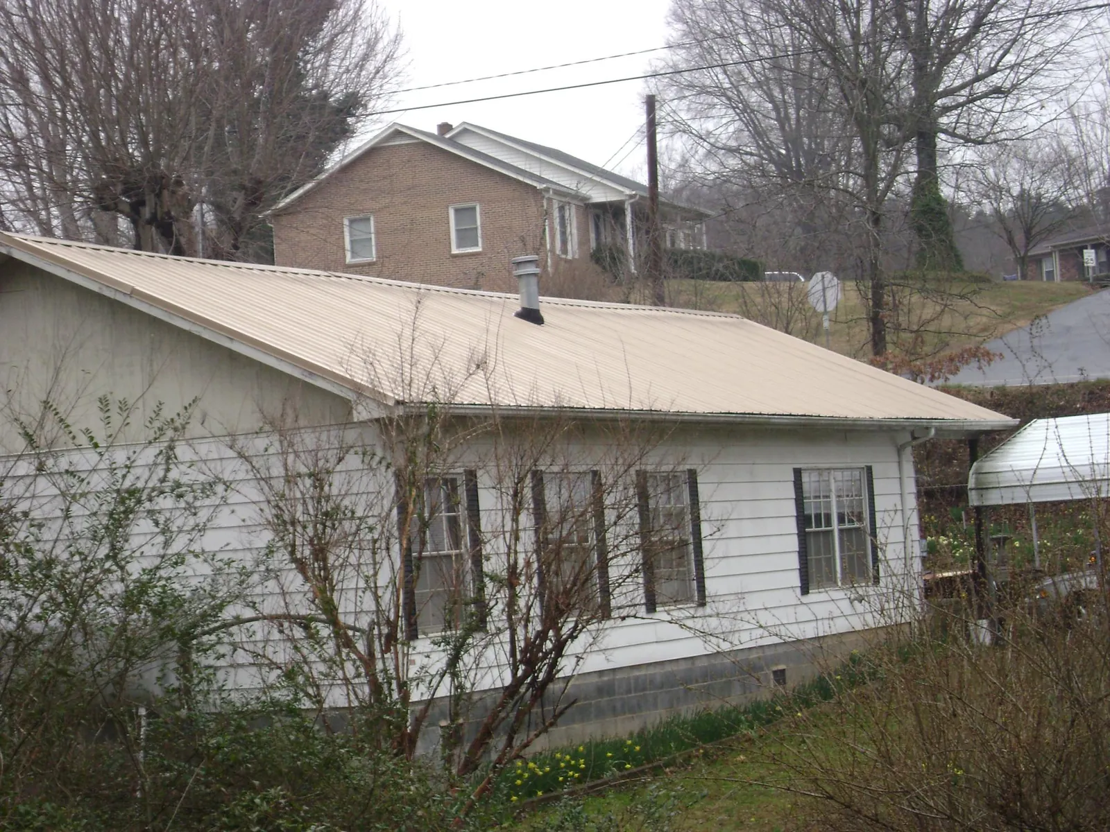 Tan metal roof on a white sided house set into a hillside — Commercial Roofing by Roofing Brothers in Shelby